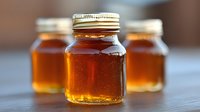 Fresh golden honey in glass jars with metal lids arranged on wooden surface, showing rich amber color and natural sweetness. Close up view with selective focus.
