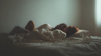 Young couple sleeping peacefully together in bed during morning hours with soft natural light creating intimate atmosphere for relationship content.