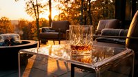 Luxury outdoor patio with whiskey glasses on table at golden hour sunset, modern furniture and fire pit in background for entertaining and relaxation.