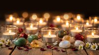 Warm candlelight creates cozy atmosphere with tea lights in glass holders, colorful Easter eggs, dried flowers and petals on rustic wooden surface for spring decor.