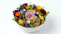 Fresh mixed salad bowl with edible flowers, colorful vegetables and greens on white background for healthy eating and gourmet cuisine concepts.