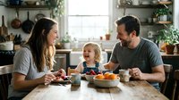 Happy young Caucasian family with toddler laughing together at breakfast table in cozy home kitchen, warm candid moment.
