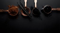 Dark chocolate ingredients arranged in copper bowls with vanilla beans on black slate background for gourmet baking and confectionery preparation.