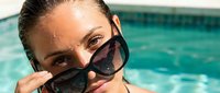 Young woman with tan skin and dark hair wearing oversized sunglasses at poolside on sunny day, perfect for summer lifestyle and vacation marketing campaigns.