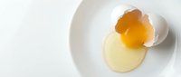 Cracked raw egg with bright orange yolk on white plate against clean background for cooking and culinary content.