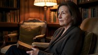 Senior woman reading book in cozy library with warm lighting and leather furniture creating peaceful evening atmosphere for relaxation and learning.