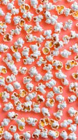 Fresh popcorn scattered on living coral background. Overhead view of white fluffy popped kernels creating modern food pattern for cinema and snack designs.