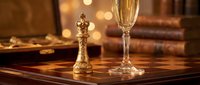 Elegant champagne flute and ornate golden chess king piece on polished wooden table with warm bokeh lights and vintage books creating luxury atmosphere.