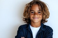 Young mixed race boy with curly brown hair and confident smile wearing denim shirt and white t-shirt against white background, arms crossed in casual pose.