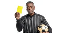 Serious African American male referee in striped shirt holding yellow card and soccer ball against white background, sport official concept.