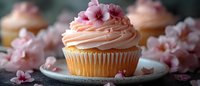 Pink frosted vanilla cupcake decorated with delicate cherry blossom flowers on vintage plate, soft focus panoramic shot with blurred background creates romantic mood.