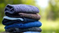 Neatly folded stack of colorful cotton towels in shades of blue and gray on blurred natural background, showing texture and softness of fresh laundry.