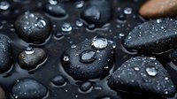 Black spa stones with water drops on dark background, macro photography showing smooth wet surface texture and natural mineral formation for wellness concept.