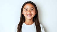 Young Asian girl with bright genuine smile wearing white t-shirt against light background, radiating happiness and confidence in casual portrait setting.