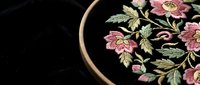 Pink floral embroidery in wooden hoop showcasing delicate needlework with roses and leaves on black fabric for crafting and textile art projects.