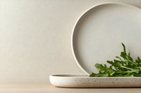 Minimalist ceramic plates with fresh arugula leaves on a wooden surface, neutral beige background for food styling and product display.