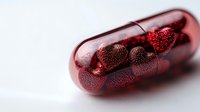 Red transparent medical capsule filled with glittering heart-shaped particles on light background, symbolizing love therapy and emotional healing concept.