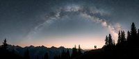 Milky Way galaxy arching over silhouetted mountain peaks and evergreen forest at night, starry sky landscape for astronomy and nature backgrounds.
