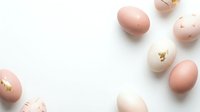 Pink and white Easter eggs with gold foil accents scattered on white background for spring holiday decorations and greeting cards.