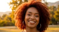 Happy young African American woman with curly hair smiling outdoors during golden hour sunset, natural beauty portrait for lifestyle and wellness content.
