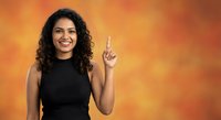 Happy young Hispanic woman with curly hair pointing up with finger gesture on orange gradient background for advertising and promotional content.