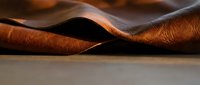 Luxurious brown leather material with rich texture and natural grain patterns, curved and folded surface creating elegant waves and shadows for craftsmanship projects.
