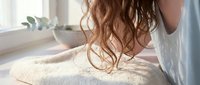 Young woman with curly auburn hair wrapped in a towel after shower, soft natural light, cozy bathroom morning routine self-care concept.