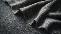 Close-up of gray herringbone wool fabric with natural folds and texture against dark background, showcasing quality textile detail for fashion design.