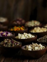 Aromatic dried flowers and herbs in wooden bowls arranged on rustic table, moody dark background with selective focus creates atmospheric composition for wellness.