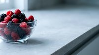 Fresh red and black raspberries and blackberries in a glass bowl on a marble countertop, ideal for food, nutrition, and healthy eating content.
