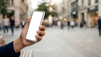 Person holding smartphone with blank white screen in urban street setting with blurred crowd and buildings in background for app mockup and mobile technology advertising.