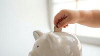Hand inserting coin into white ceramic piggy bank for savings and financial planning goals.