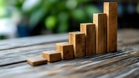 Wooden blocks arranged as ascending stairs or growing bar graph on rustic table, symbolizing business growth, progress and success in finance.