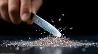 Dramatic macro shot of knife blade crushing and scattering pink salt crystals against dark background with dynamic motion blur and sparkling light reflections.