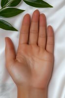 Open palm of a light brown skin tone hand against white fabric background with green leaves, suitable for wellness and healthcare concepts.