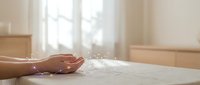 Woman's hand resting on wooden table with soft natural light streaming through window, conveying calm, mindfulness, and peaceful moments for wellness and lifestyle content.