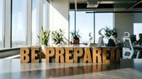 BE PREPARED wooden letters on office desk with blurred business team meeting in background, motivational workplace concept for readiness and strategic planning.