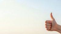 Hand showing thumbs up gesture against soft pastel sky background expressing approval, success and positive feedback for business presentations.