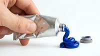 Hand squeezing blue acrylic paint from metal tube onto white surface for art projects and creative painting activities.