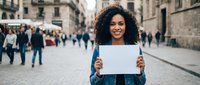 Young African American woman holding blank white paper sign on busy urban street for advertising mockup and promotional campaigns.