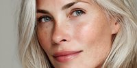 Close-up portrait of confident blonde Caucasian woman with natural makeup and glowing skin looking directly at camera with serene expression.