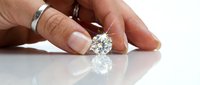 Caucasian hand holding a sparkling round brilliant cut diamond, reflecting light on a white surface, luxury gemstone concept.