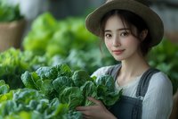 Young Asian woman in straw hat and overalls holding fresh leafy greens in garden setting, representing sustainable farming and organic produce.