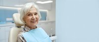 Senior Caucasian woman smiling in dental chair wearing protective bib at modern clinic office for oral health checkup and preventive care treatment.