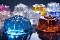 Colorful translucent gelatin desserts in decorative molded shapes arranged on reflective surface with dramatic lighting for culinary photography.