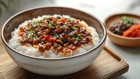 Savory minced meat with vegetables served over steamed white rice in ceramic bowl, garnished with green onions and sesame seeds, Asian cuisine style meal.