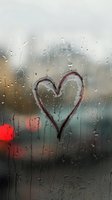 Heart drawn on rainy window glass with water drops streaming down, blurred city lights in background creating moody romantic atmosphere.