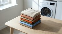 Stack of neatly folded colorful towels on wooden table in modern laundry room with white washing machine. Clean household linens ready for storage.