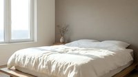 Minimalist bedroom with unmade bed featuring white linens, wooden platform frame, and natural light from large window, suitable for interior design and home decor projects.
