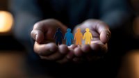 Caring hands holding colorful paper cutout figures symbolizing diversity, unity and community support against dark background with soft bokeh lights.